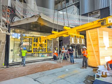 Eine konkav gebogene Glasscheibe wird präzise unter einem Gebäudevorsprung positioniert und montiert. Bildrechte: Heavydrive.com